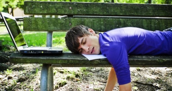 Person sleeping on bench with laptop.